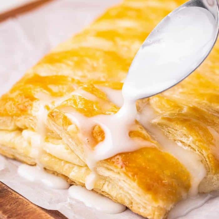 using spoon to drizzle glaze on lemon cream cheese danish