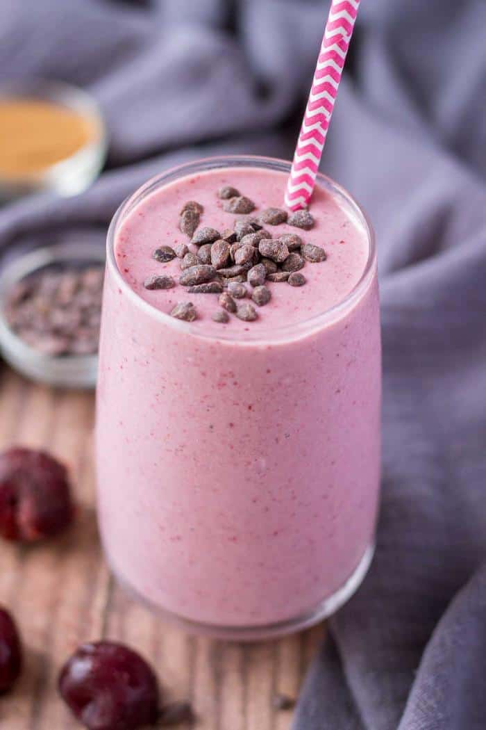 cherry banana smoothie in tall glass with straw and cacao nibs